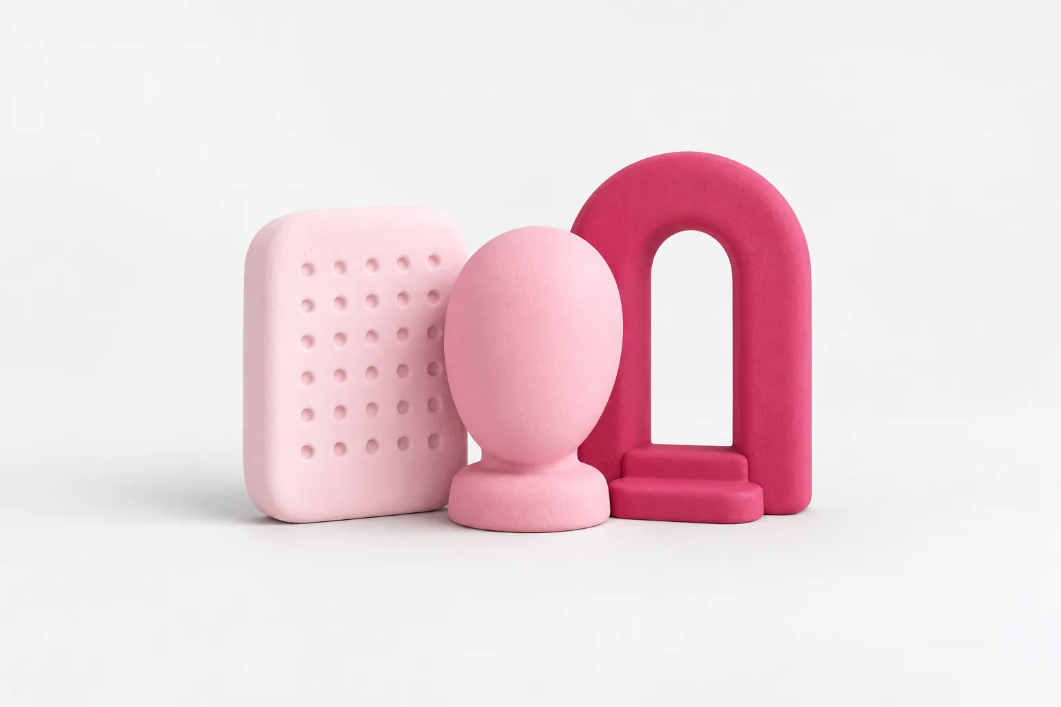 Three matte clay objects in rose tones: a pale block with a grid of dimples, a smooth faceless oval mask on a short stand, and a rounded archway with one small step